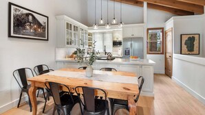 A modern kitchen with white cabinets, a wooden dining table, and hanging pendant lights. - Gold Bend Bliss (Truckee)
