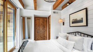 A bedroom with a large bed, wooden doors, and a window with curtains. - Gold Bend Bliss (Truckee)