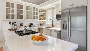A modern kitchen with white cabinetry, a stainless steel refrigerator, a gas stove, and a bowl of fruit on the island. - Gold Bend Bliss (Truckee)