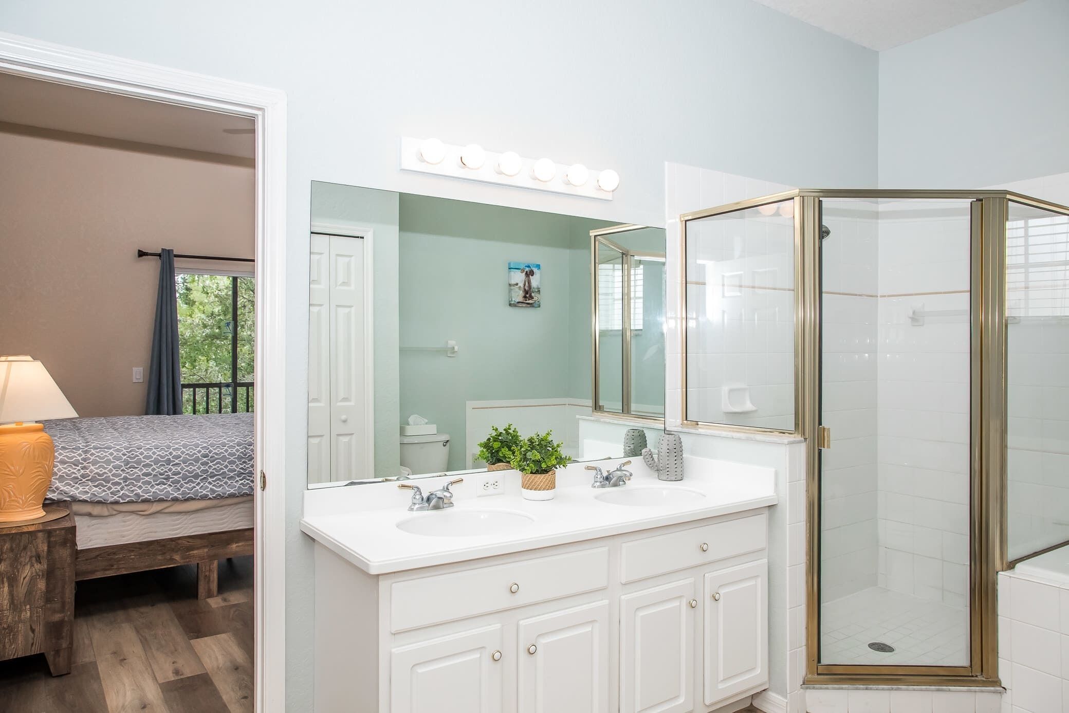 A bathroom with a white vanity, a glass shower enclosure, and a mirror with lights above it.