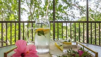 A glass pitcher and two glasses of iced tea with lemon slices on a tray, set on a balcony with a railing and greenery in the background.