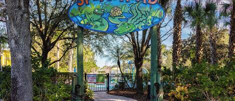 A sign for Splashpad with a pathway leading to it, surrounded by trees.