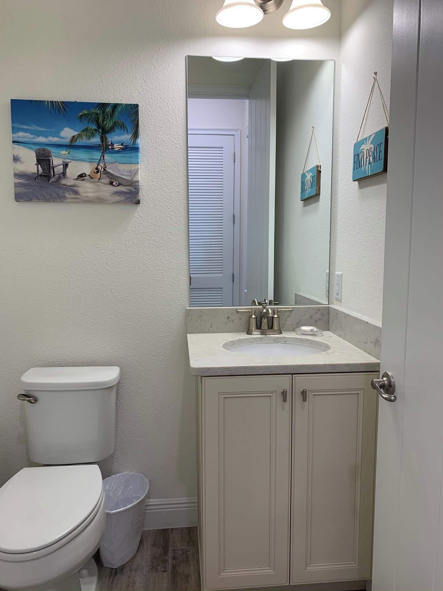A bathroom with a toilet, sink, and mirror. There is a painting of a beach scene on the wall.