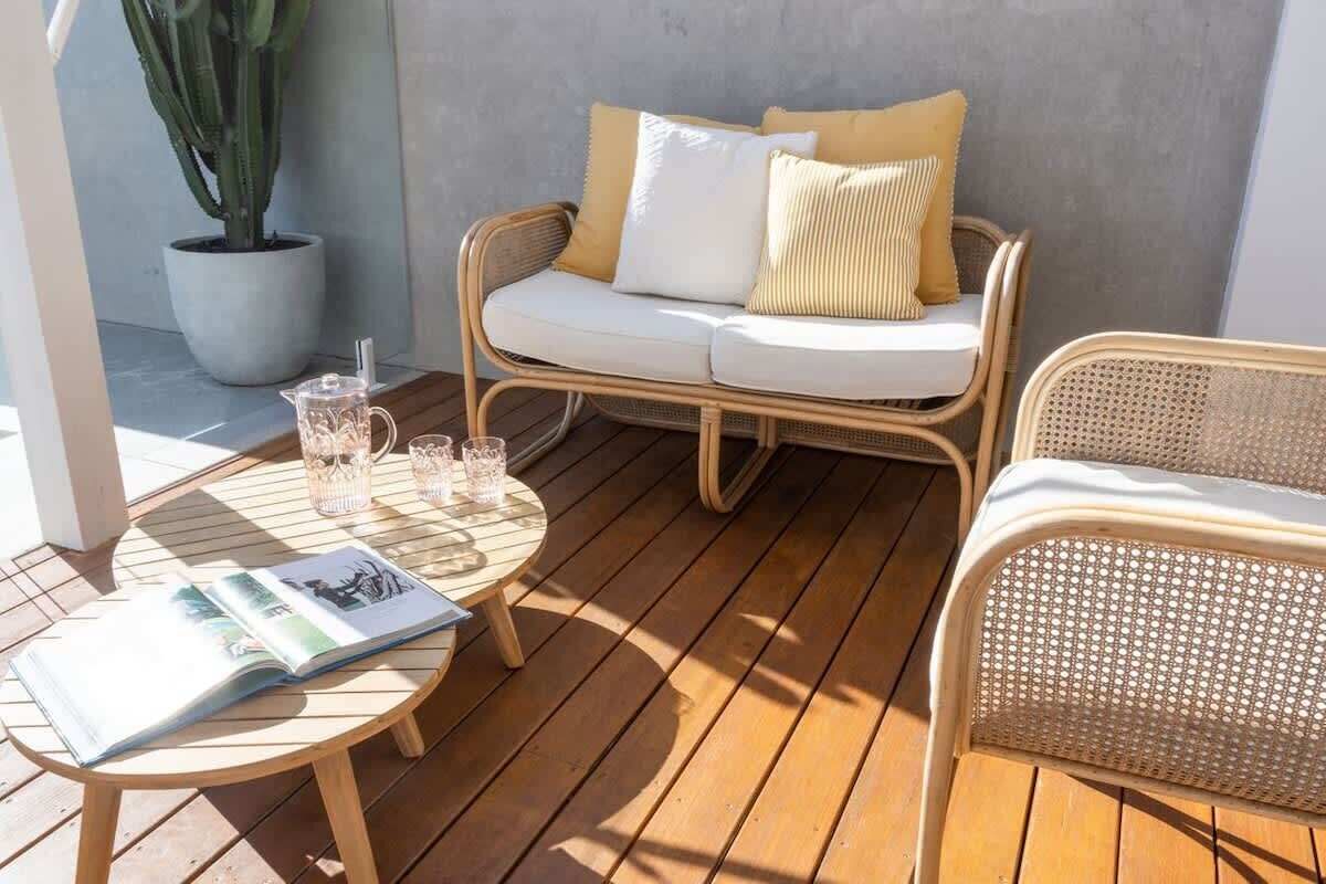 Una terraza de madera con un sofá de mimbre, una mesa redonda y una planta en maceta.