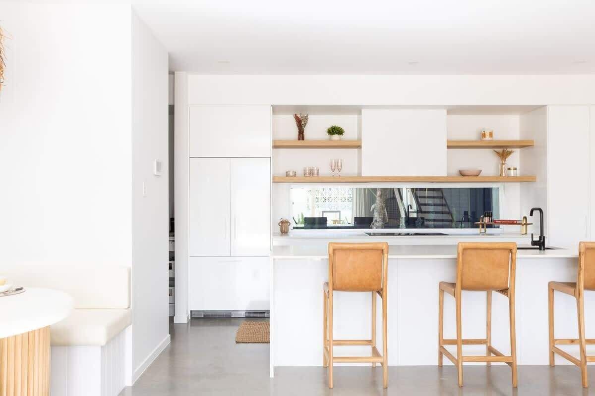 A modern kitchen with white cabinetry, wooden bar stools, and a central island with a sink.
