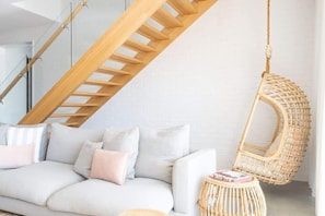 A modern living room with a sofa, cushions, a hanging chair, and a staircase.