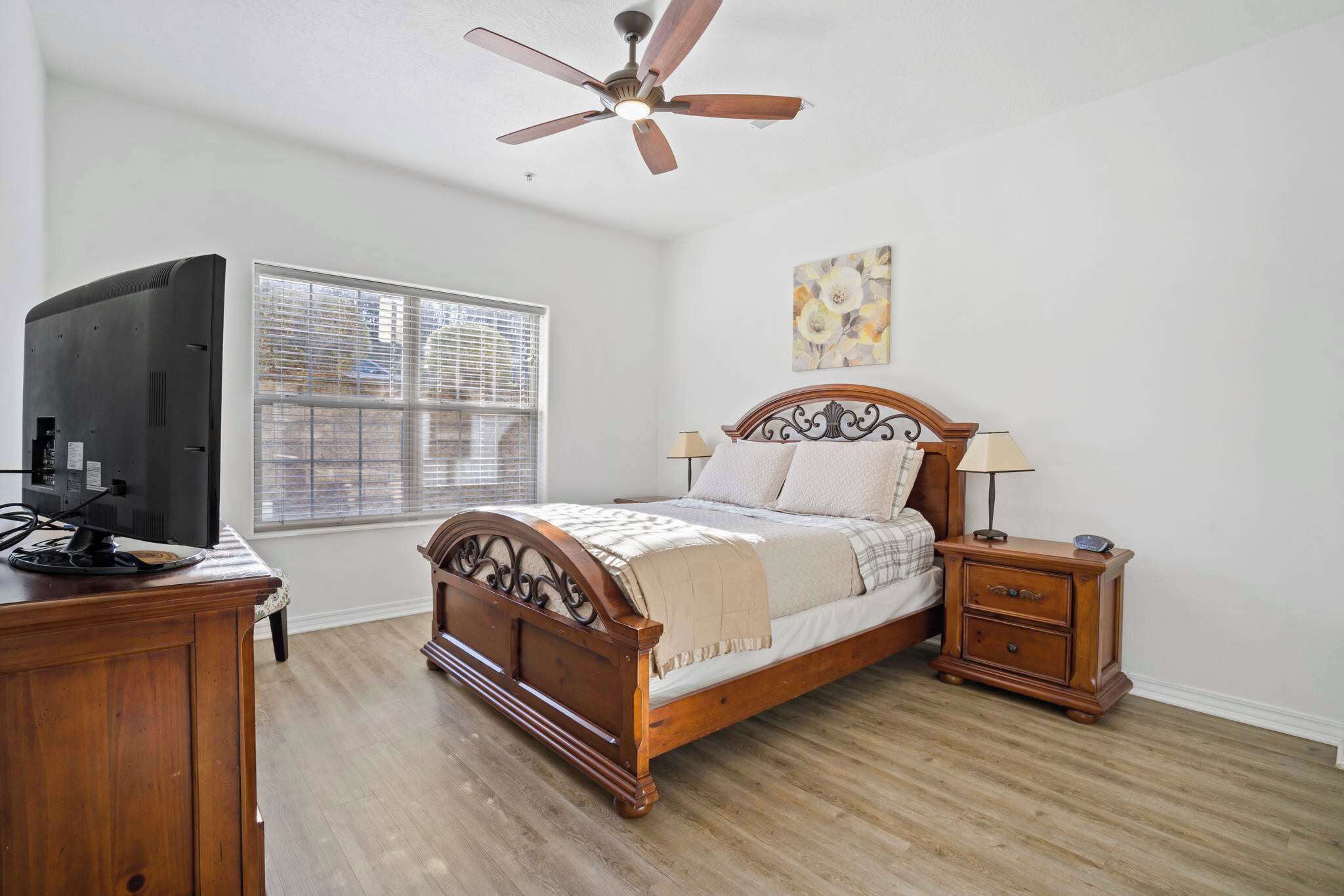 A bedroom with a wooden bed, a nightstand, a TV, and a ceiling fan.
