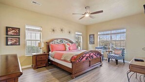 A bedroom with a wooden bed, a ceiling fan, a window with blinds, a small table, and a chair. - Lakefront Sanctuary - Table Rock Lake Adventures (Branson)