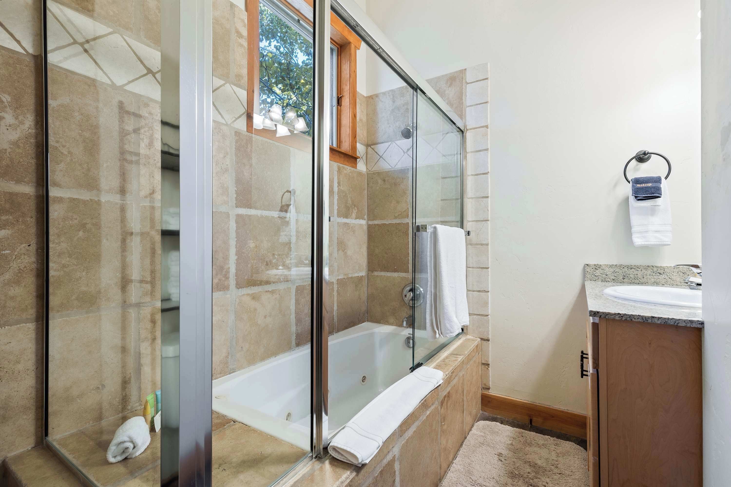 Un bagno moderno con doccia vetro, vasca freestanding e mobile bagno in legno con lavabo.