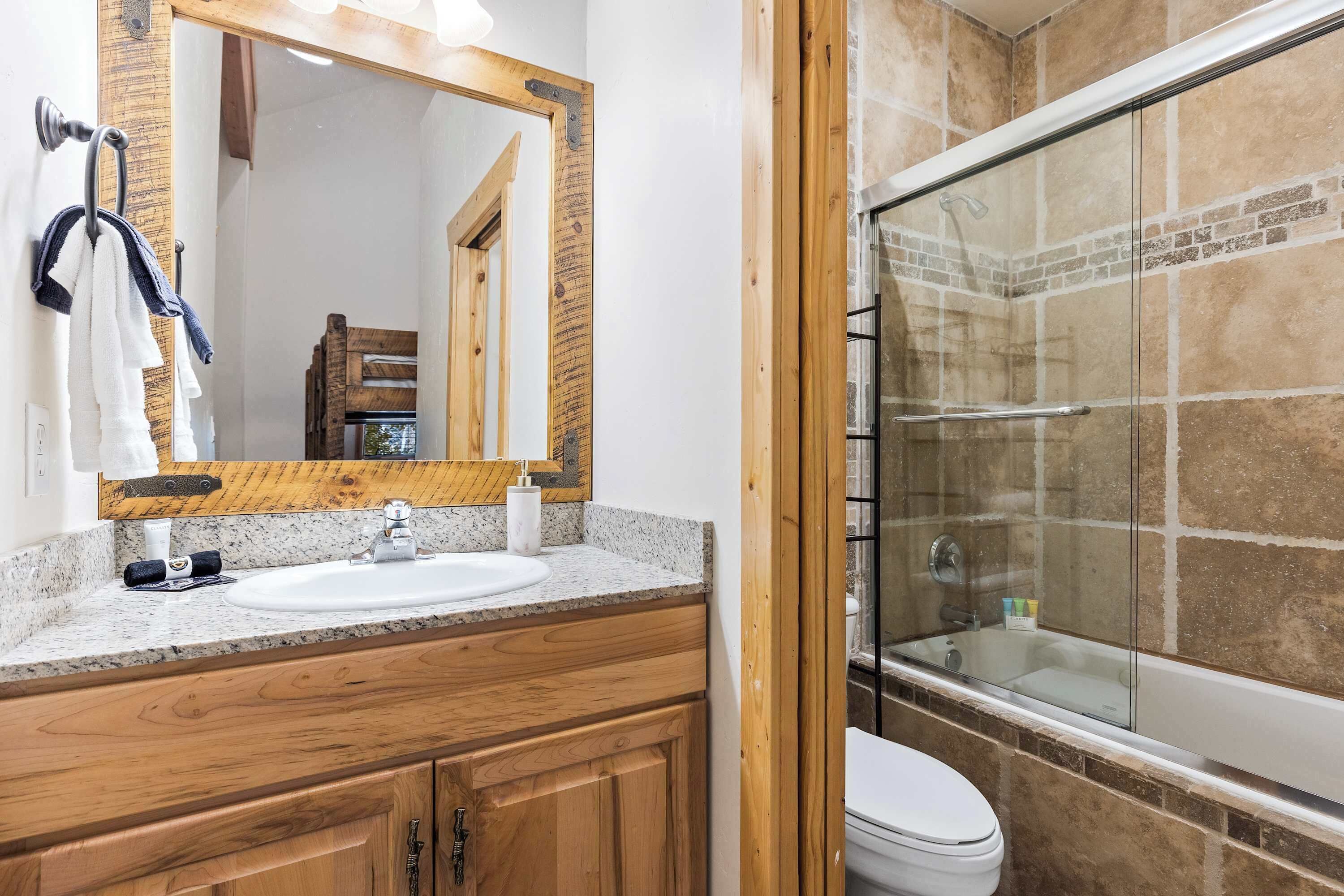 Un baño con tocador de madera, lavamanos, espejo y cabina de ducha con puertas de cristal.