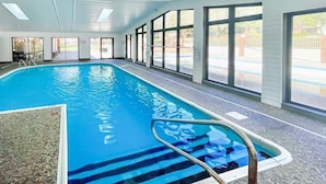 En indendørs swimmingpool med glasvægge, flisegulv og en metalstige.