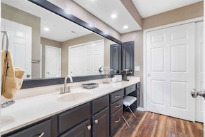 Une salle de bain moderne avec un grand miroir, un lavabo, des meubles sombres et un banc.