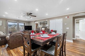 A dining area with a wooden table set for four, a ceiling fan, and a view of the outside through large windows.