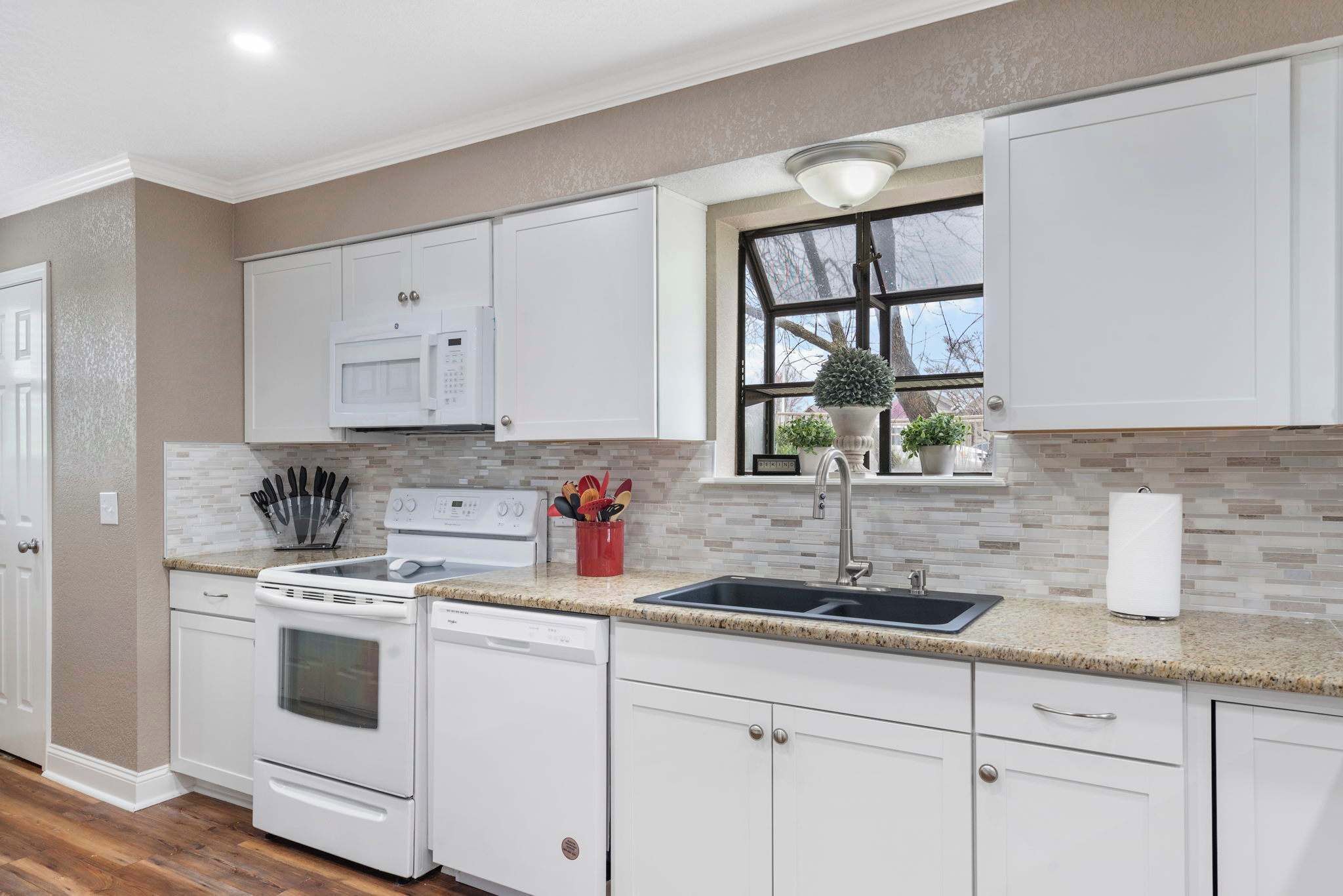 A modern kitchen with white cabinetry, a granite countertop, a built-in microwave, and a window with a view.