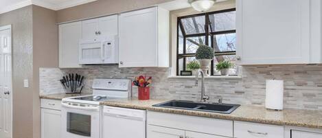 A modern kitchen with white cabinetry, a granite countertop, a built-in microwave, and a window with a view.