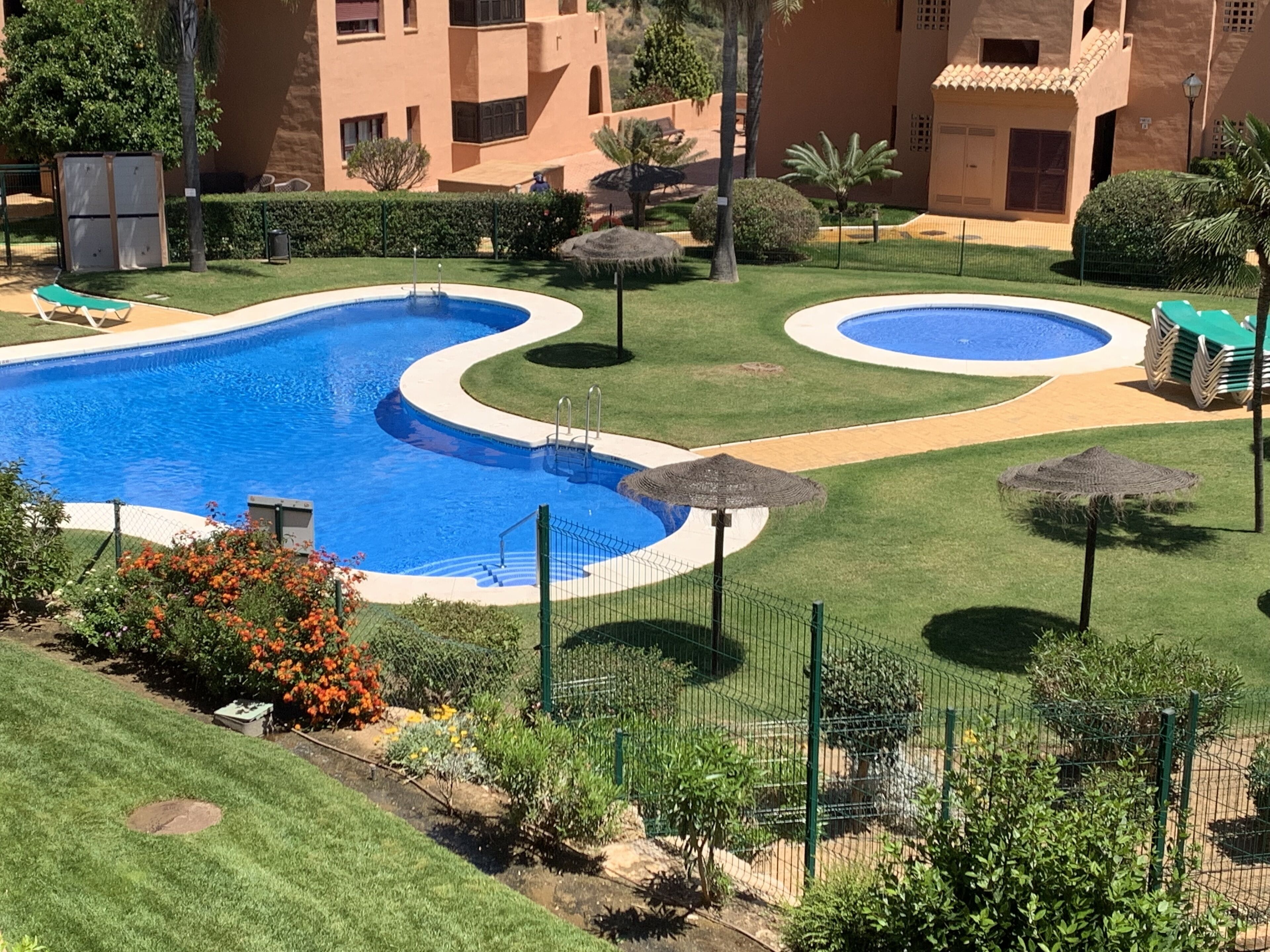 Ein Poolbereich mit zwei Pools, umgeben von gepflegtem Rasen und Palmen.