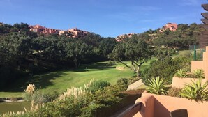 A golf course with a pond, surrounded by lush greenery and residential buildings in the background.