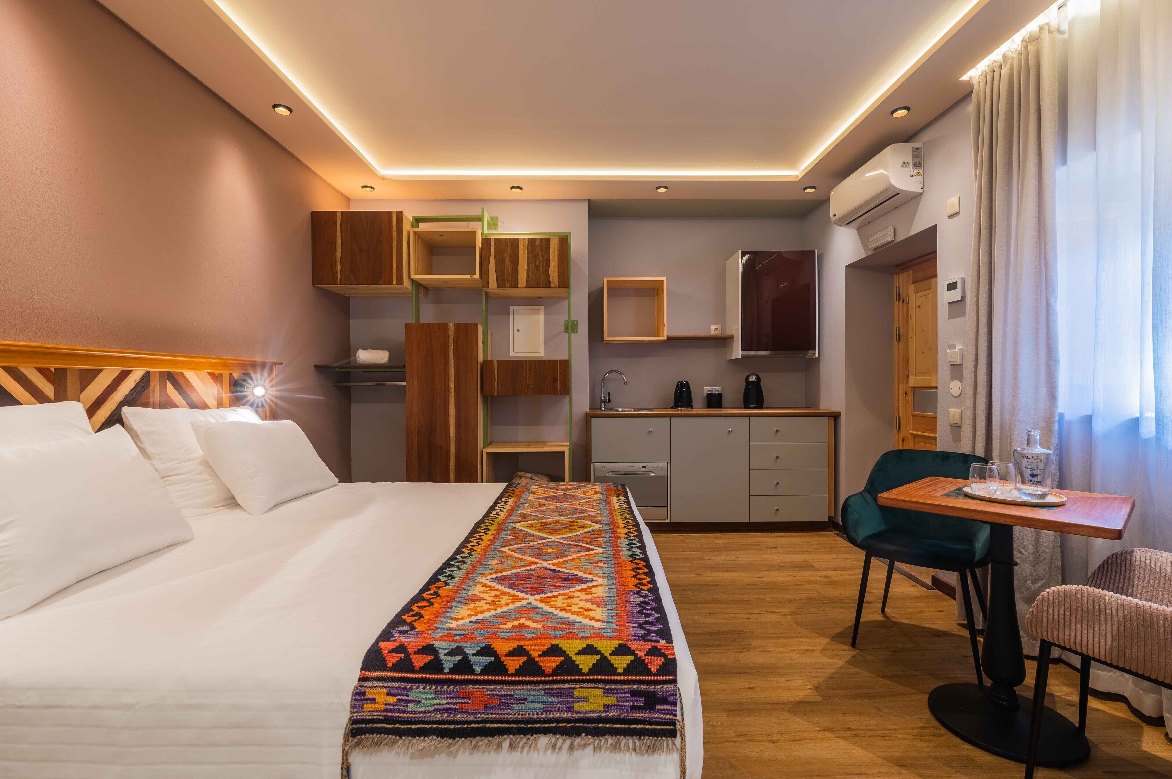 Habitación de hotel con cama, escritorio con silla, kitchenette y televisor.