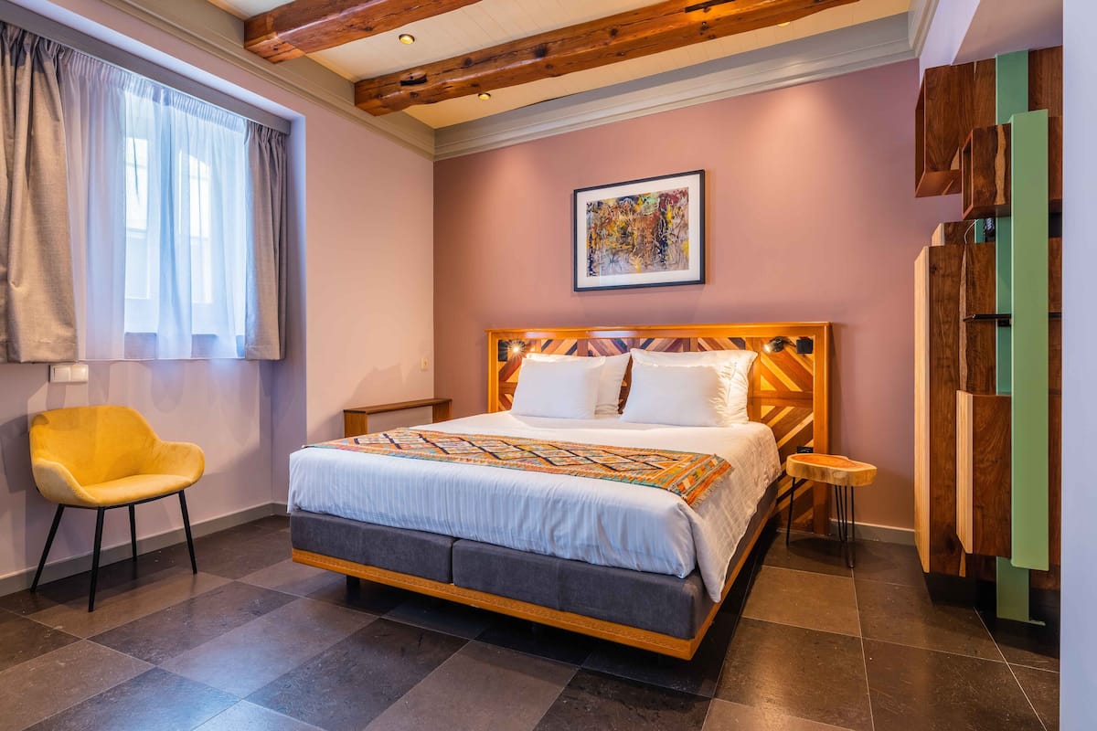 Un dormitorio con cama, una silla, una mesita pequeña, un cuadro en la pared y muebles de almacenamiento de madera.