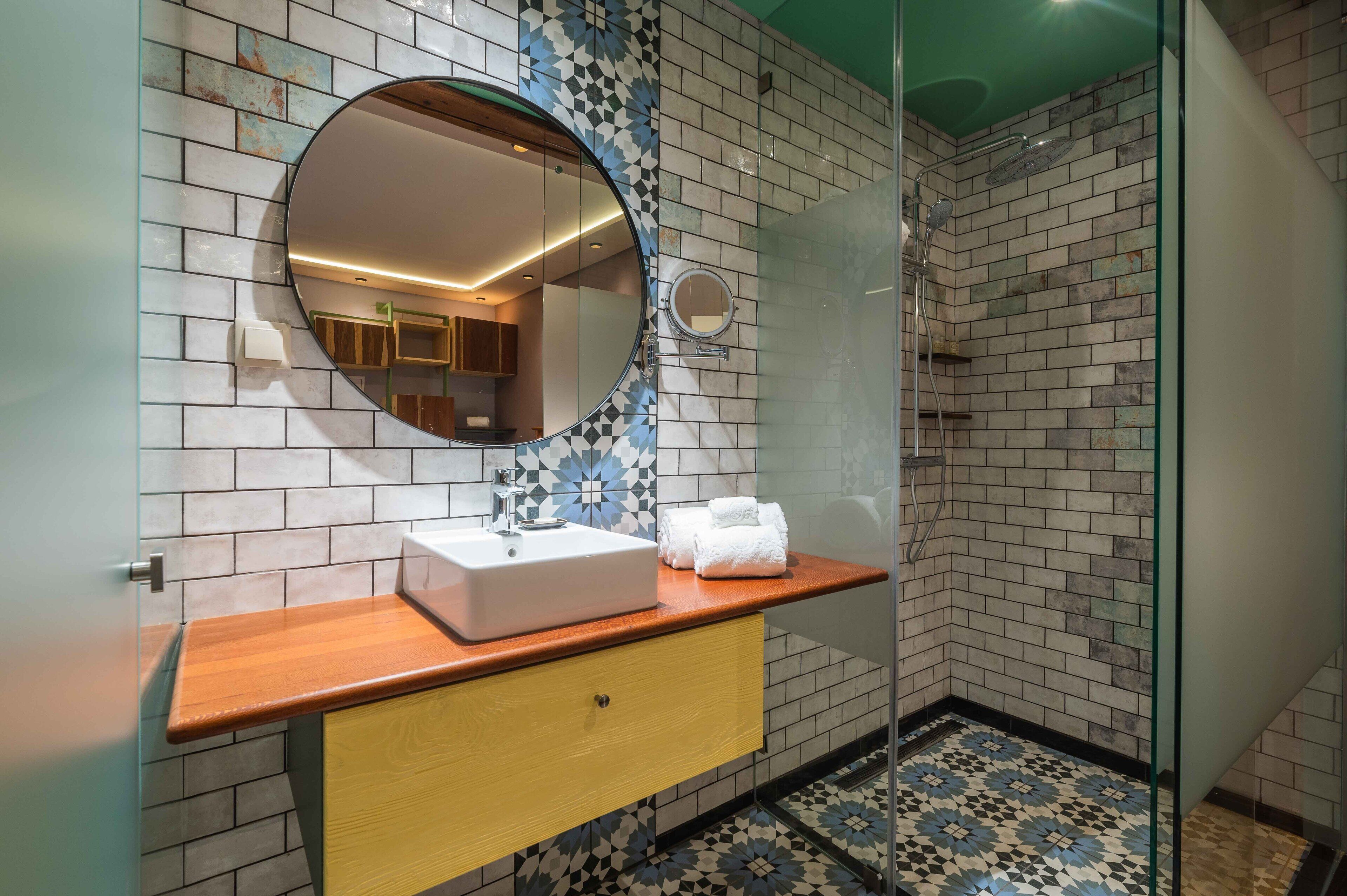 A bathroom with a wooden vanity, a round mirror, and a shower area with a glass door.