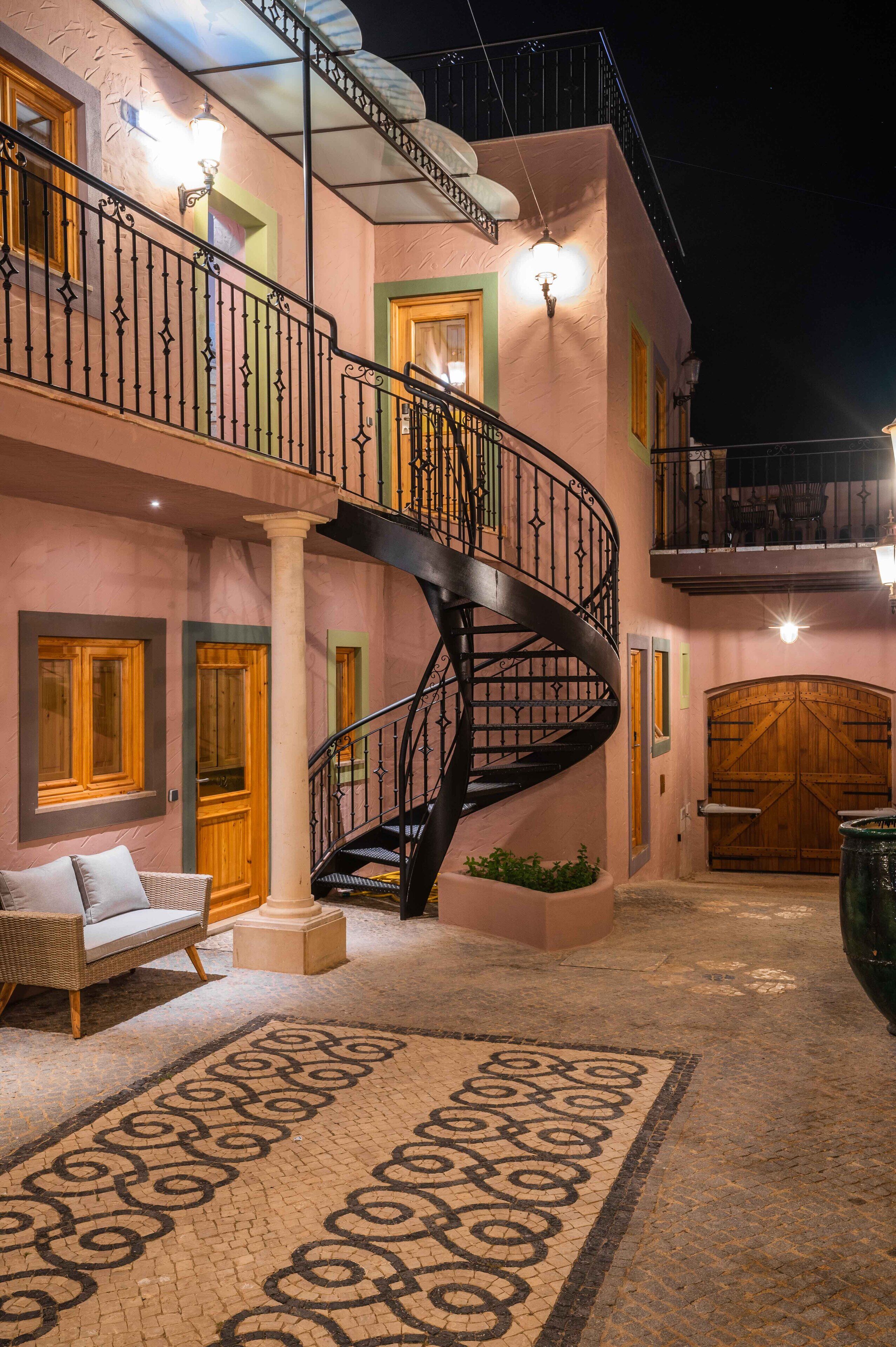 A pink building with a spiral staircase, wooden doors, and a wrought iron railing.