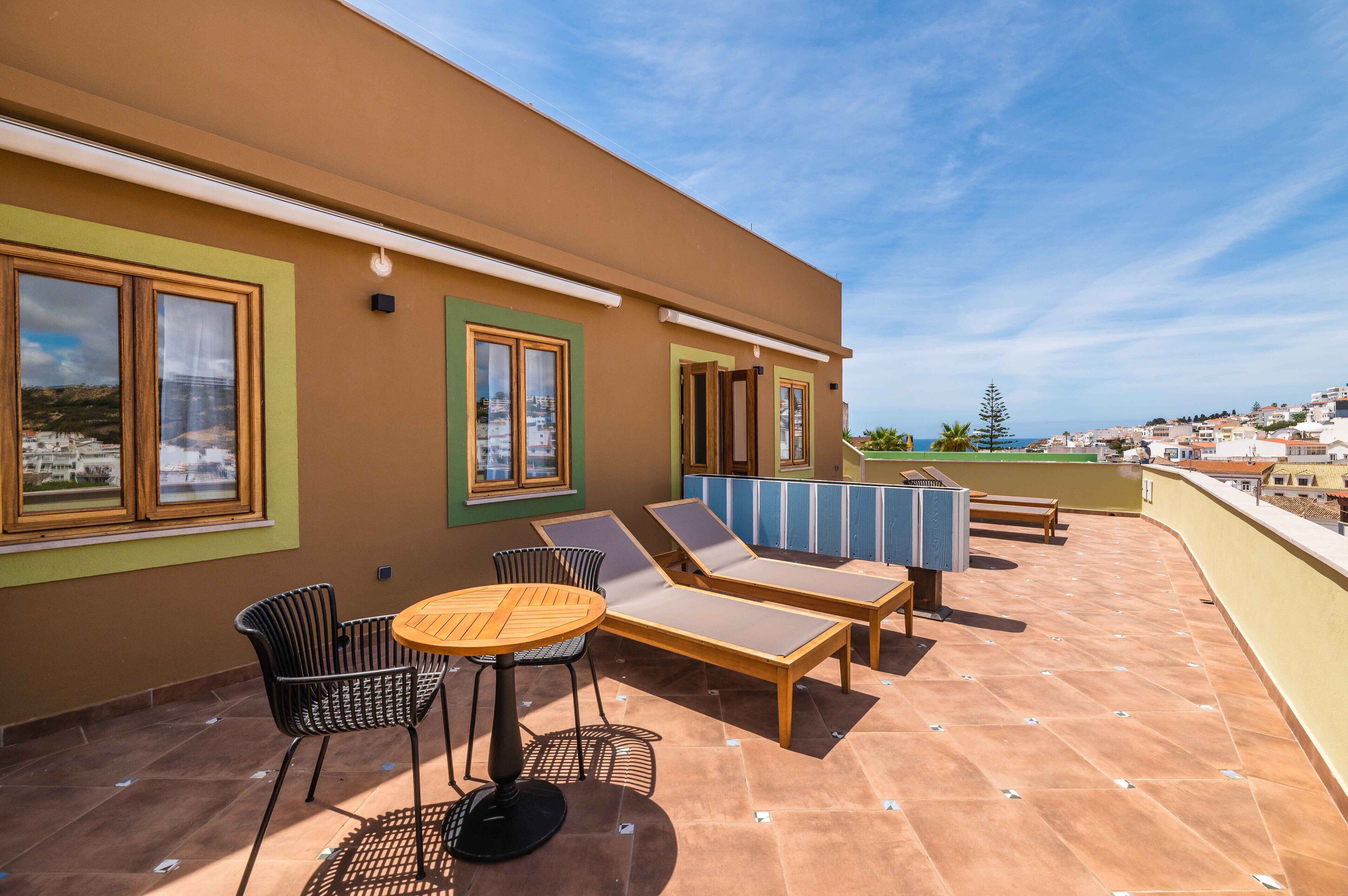 Una terraza en la azotea con mesa y sillas, sillones de descanso y vistas a la ciudad.