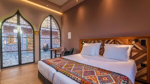 A hotel room with a large bed, a patterned throw blanket, and a view through a window with decorative ironwork. - Vila Origens Boutique Hotel Albufeira (Albufeira)