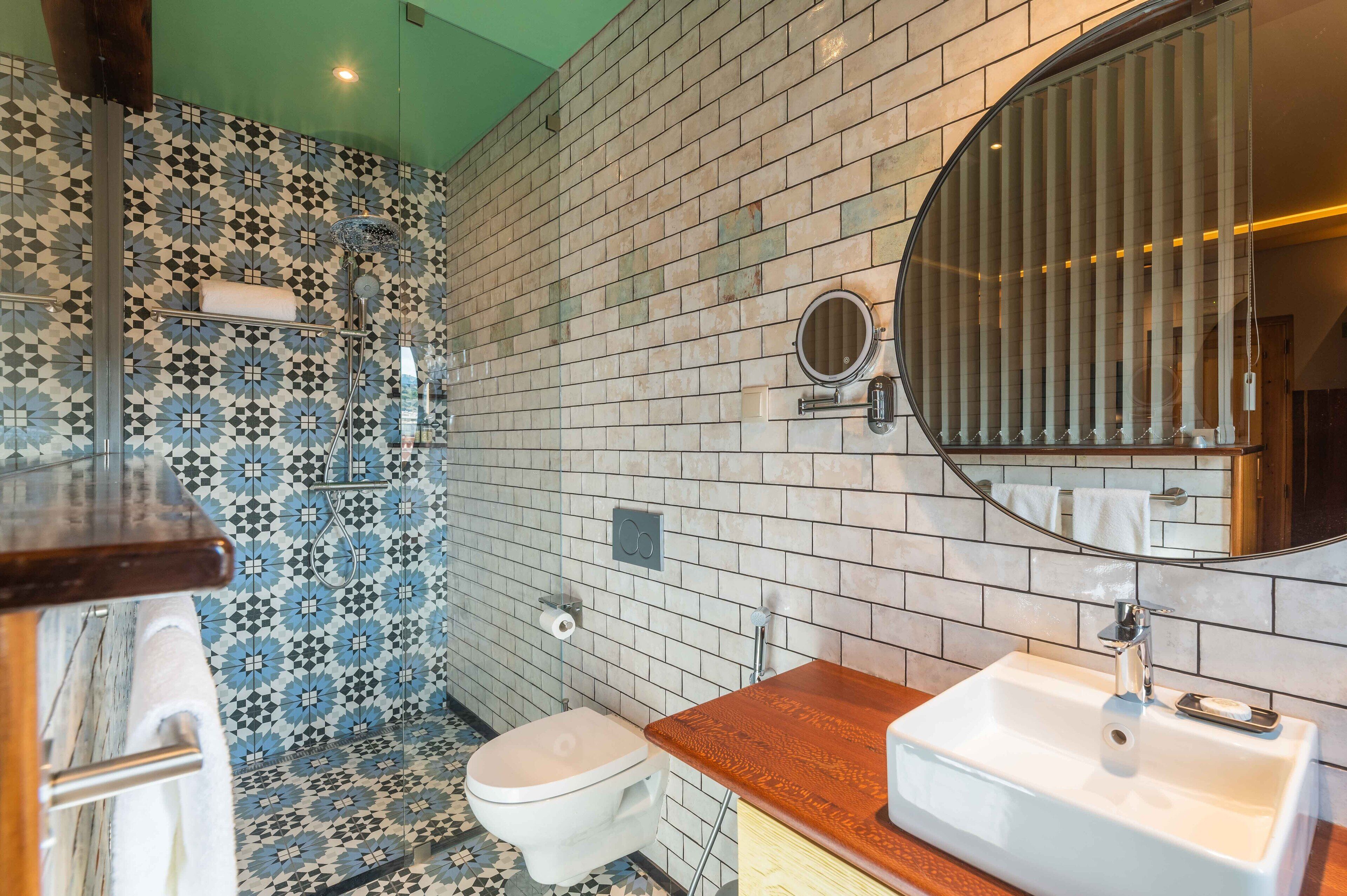 A bathroom with a patterned tile wall, a toilet, a sink with a mirror, and a shower area.