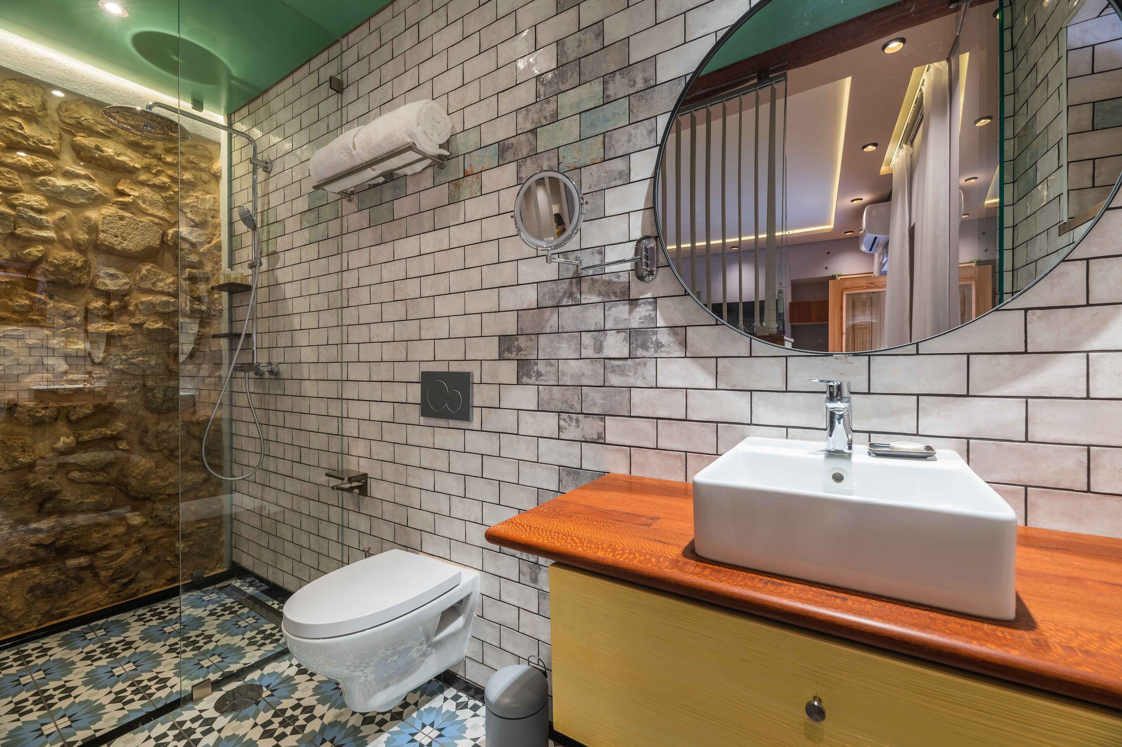 Un baño con pared de piedra, suelo de baldosas, inodoro, lavabo y espejo.