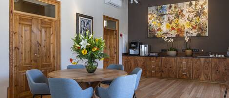 A modern kitchen with wooden cabinets, a dining table with chairs, and a large abstract painting on the wall.
