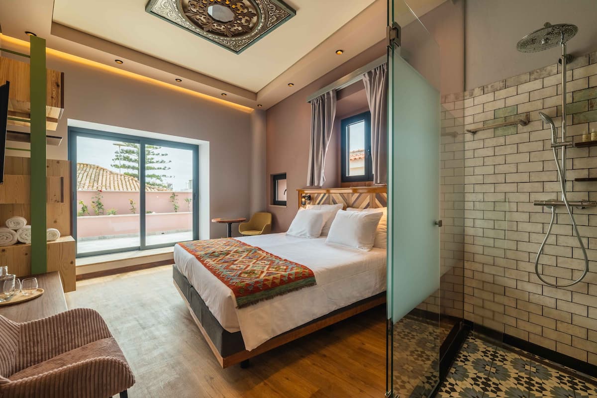 Habitación de hotel con una cama grande, ducha, vistas al exterior y una mesita con toallas.