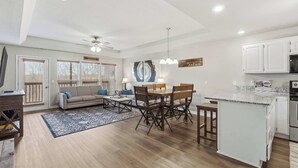 Une cuisine moderne avec des meubles blancs, un coin repas avec une table et des chaises en bois, et un salon avec un canapé et une table basse.