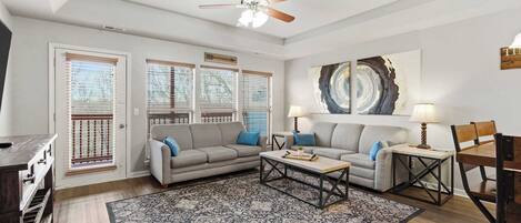 A living room with two sofas, a coffee table, a dining table with chairs, a ceiling fan, and a large abstract painting on the wall.