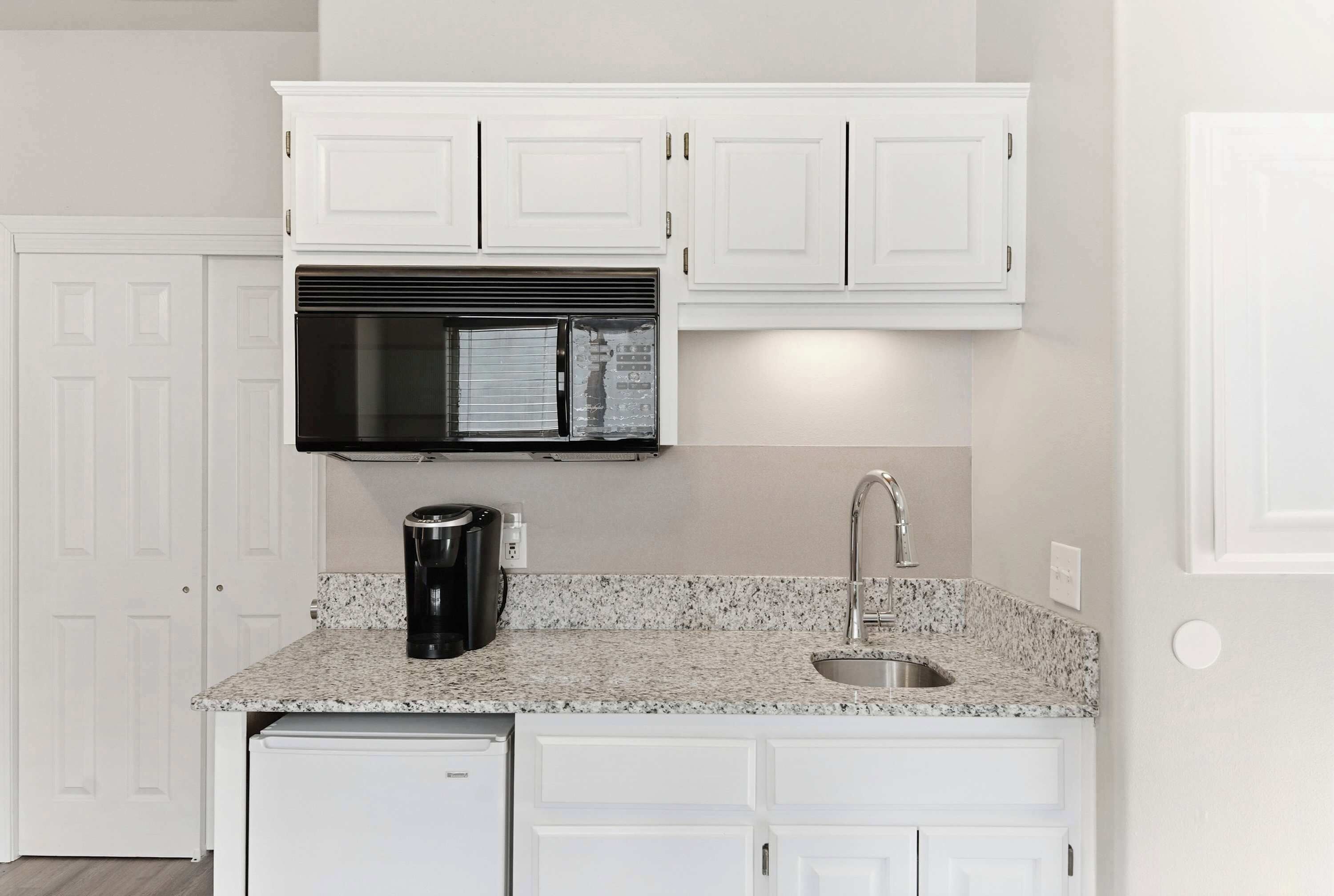 A kitchen with white cabinets, a black microwave, a coffee maker, and a sink.