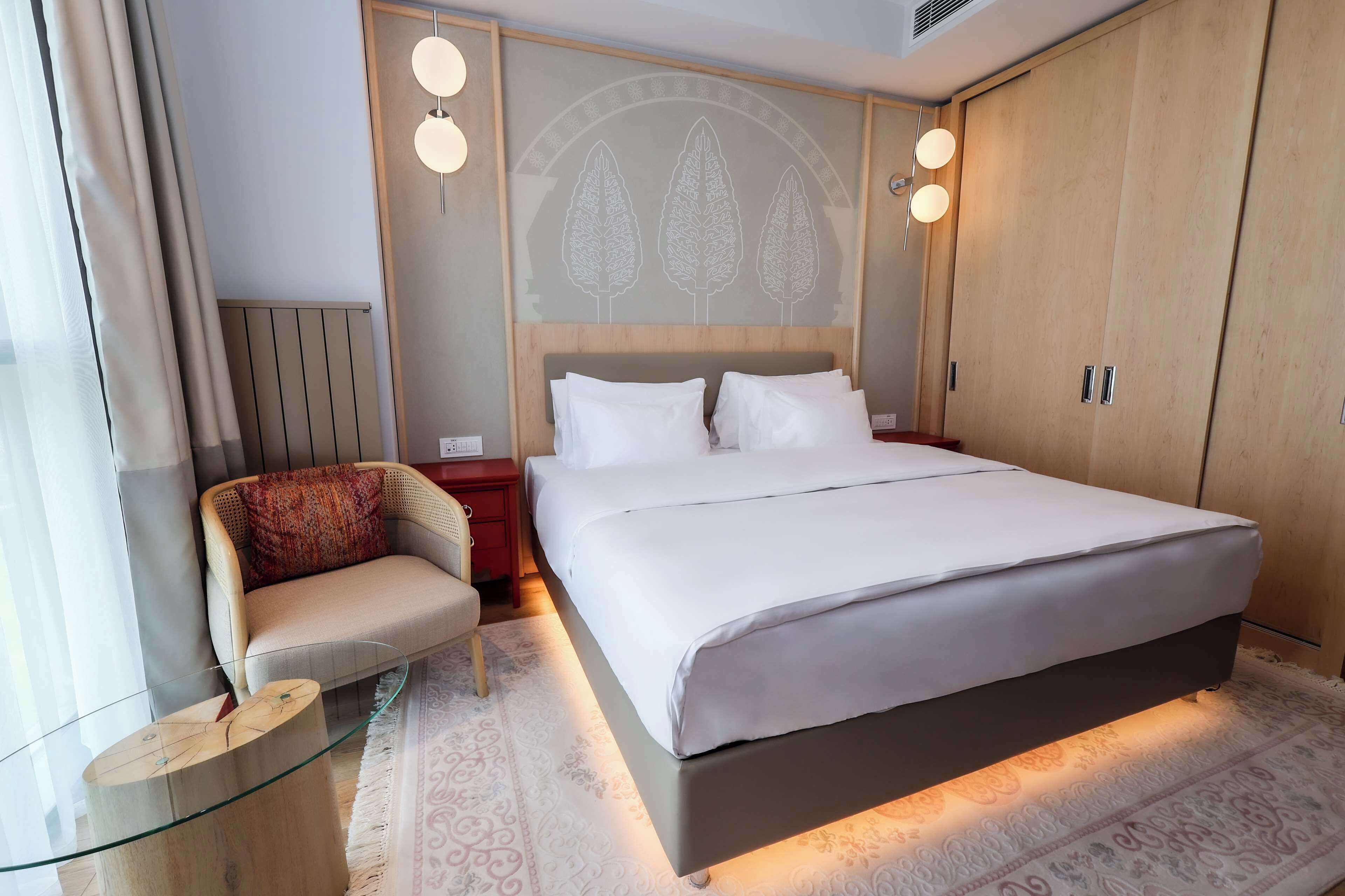 A modern bedroom with a large bed, a chair, a bedside table, and a wardrobe.