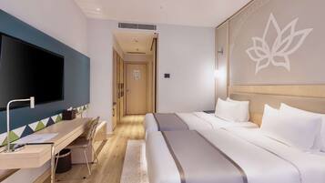 A hotel room with a bed, a desk with a chair, a television, and a wall with a lotus flower design.