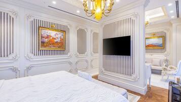 A luxurious bedroom with a large bed, a flat-screen TV, ornate wall decorations, and a chandelier.