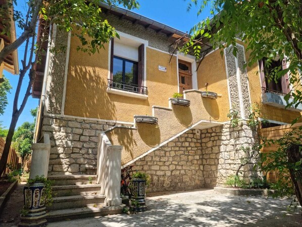 Un bâtiment doté d’une façade en pierre, d’un balcon avec une rambarde en métal et d’un escalier menant à l’entrée.