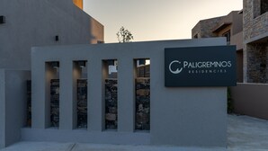 En moderne bygning med skiltning for Paligremnos Residencies. Facaden er i sten med rektangulære åbninger og et fladt tag.