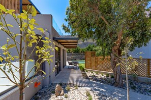 A modern outdoor patio with a pool, a wooden pergola, and a rock garden.