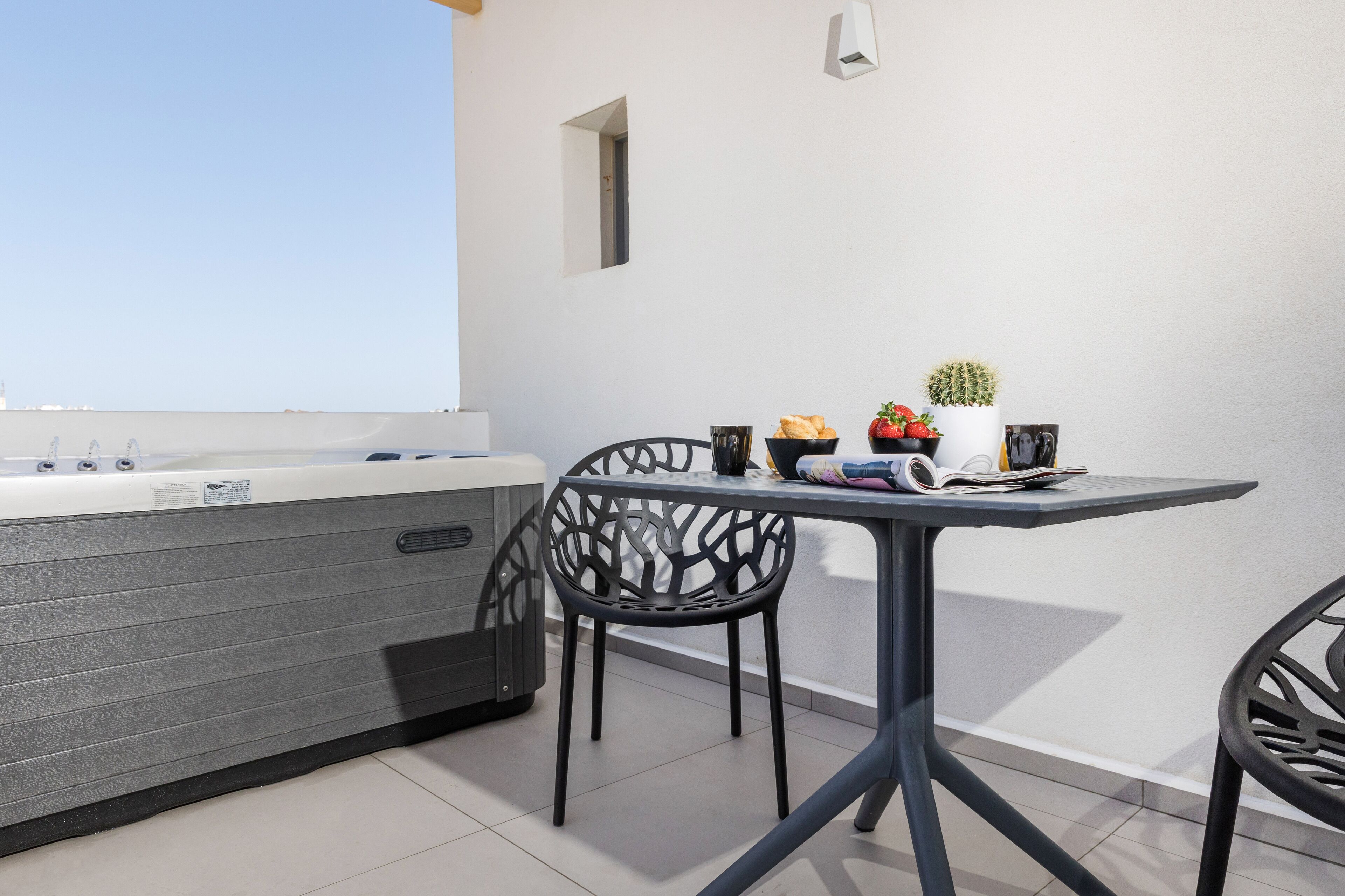A modern outdoor seating area with a table and chairs, a hot tub, and a small potted plant.