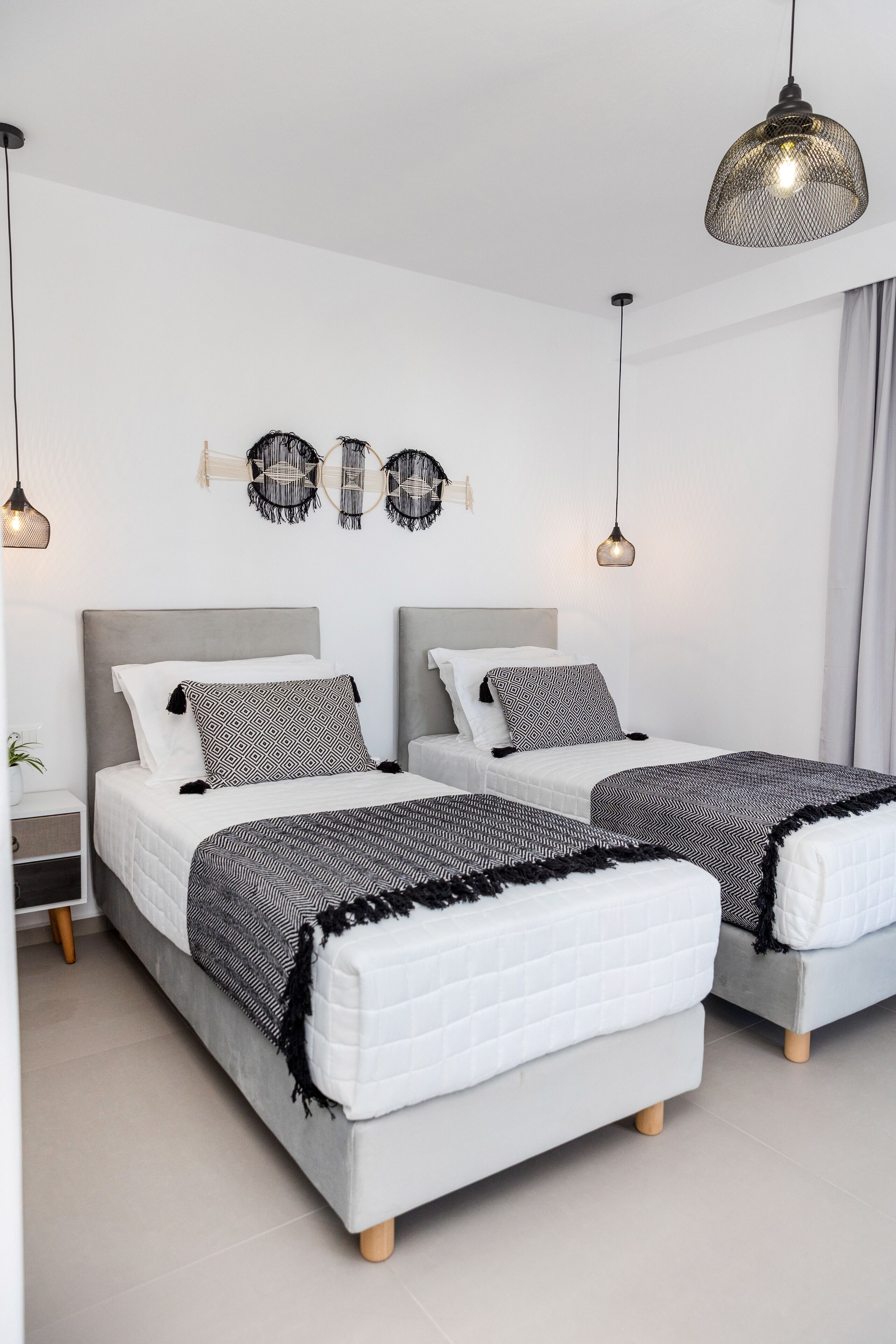 A modern bedroom with two beds, a hanging light fixture, and a wall-mounted decorative piece.