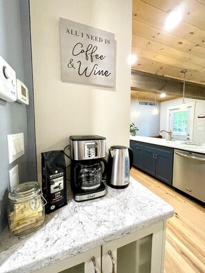 A kitchen with a coffee maker, a kettle, and a bag of coffee on the counter.