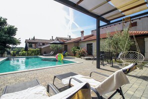 A swimming pool with lounge chairs and a hanging chair, surrounded by a patio area with a covered section. - Mani in Pilkovići - Istria / Mani in Pilkovići - Apartment for 6 people (Kanfanar)