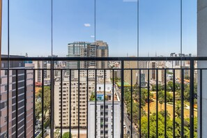 Um edifício alto com vários andares, janelas amplas e vista para um horizonte urbano com outros edifícios e um parque.