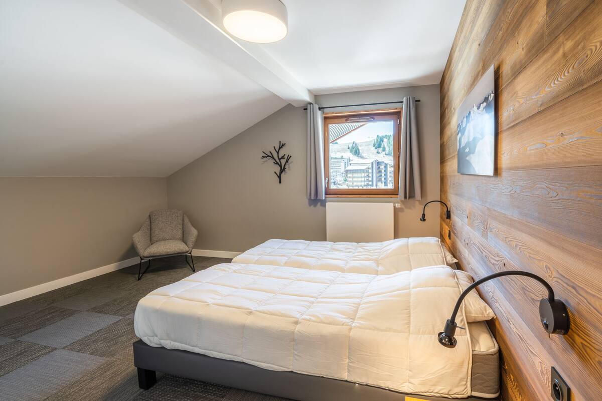 Une chambre à coucher avec un lit, une chaise, une fenêtre donnant sur un beau paysage et un lambris en bois.