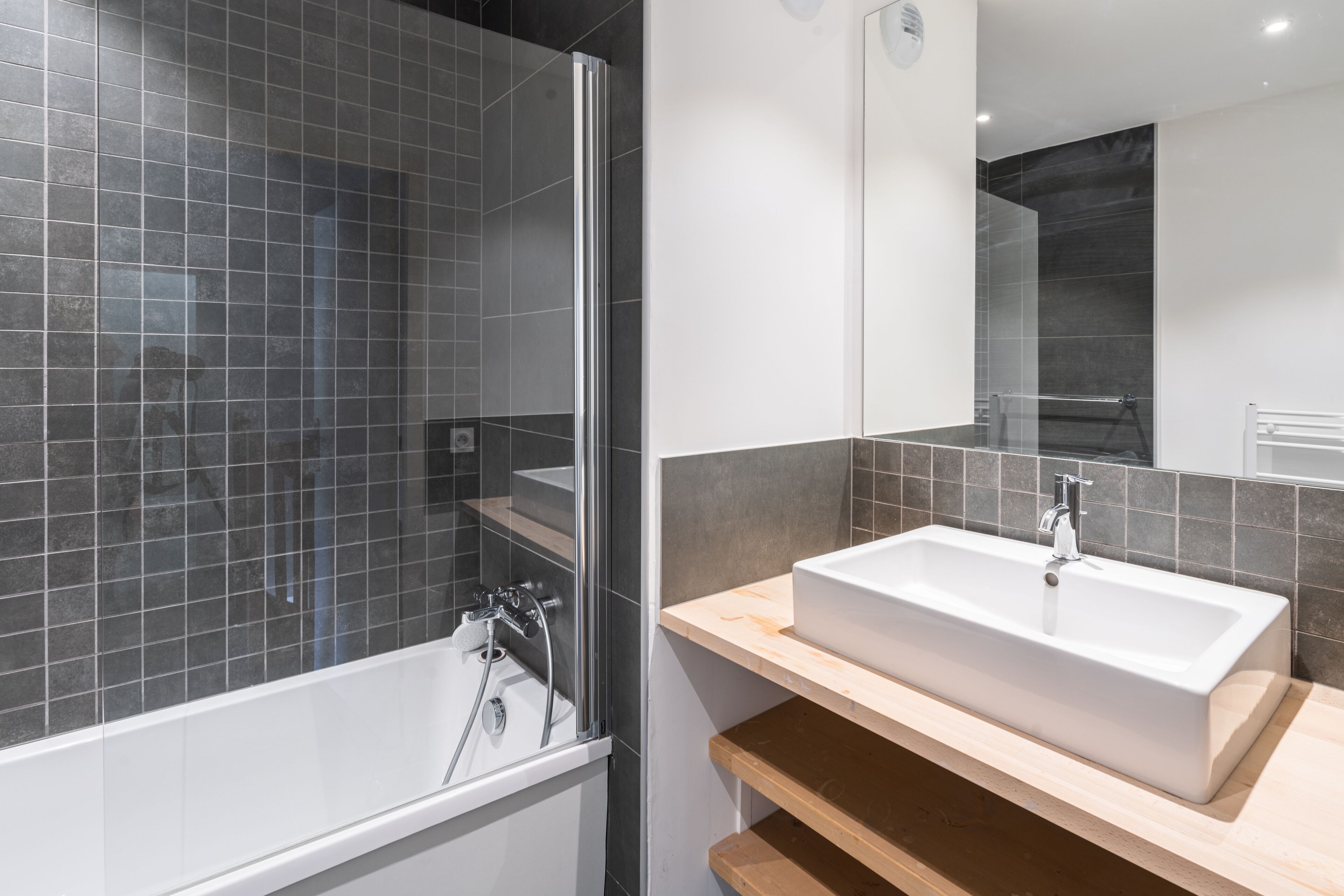 Un baño moderno con ducha de vidrio, lavamanos blanco y tocador de madera.