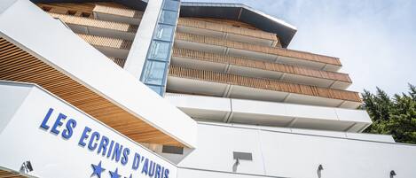 Un bâtiment moderne, sur lequel on peut lire l’inscription « LES ÉCRINS D’AURIS », et doté d’une série de balcons avec des persiennes en bois.