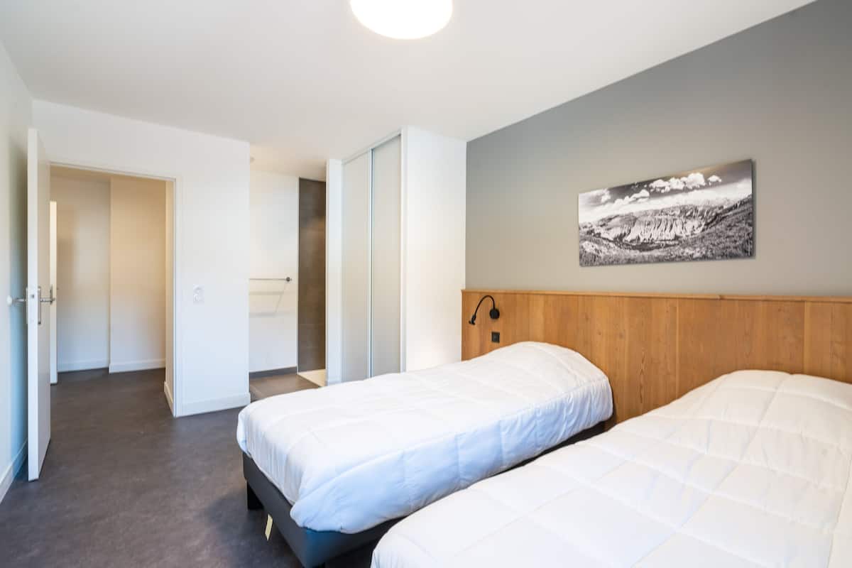 Une chambre d’hôtel avec deux lits, une tête de lit en bois, un tableau accroché au mur et une porte donnant sur une autre pièce.