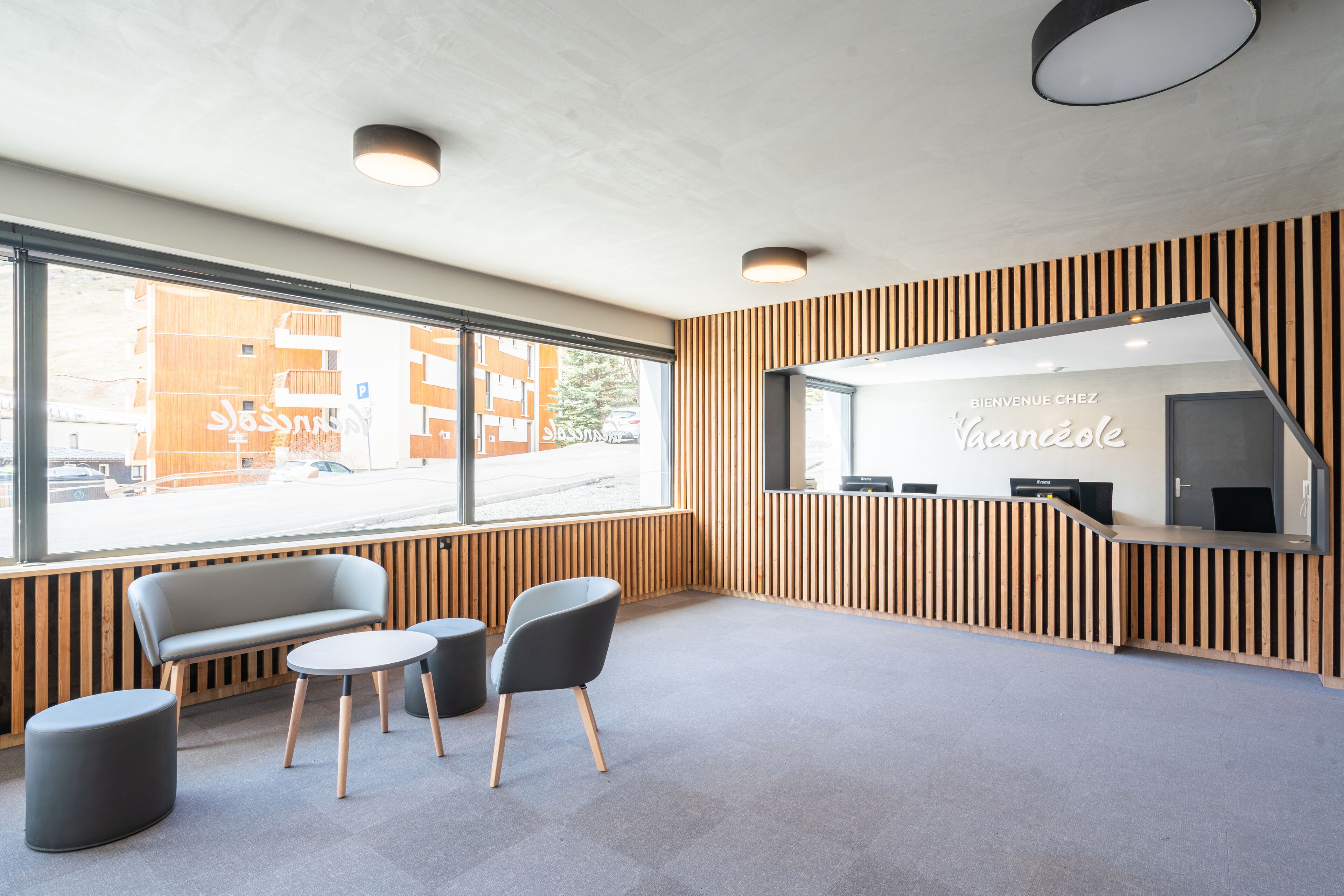 A reception area with a wooden panel wall, a reception desk, a seating area with a bench and two chairs, and a large window offering a view of the street.